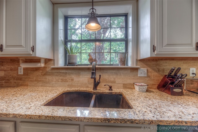 kitchen featuring light stone counters, white cabinets, hanging light fixtures, and sink