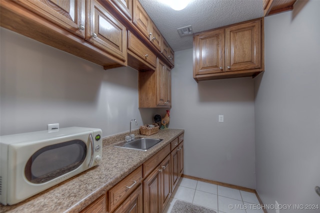 laundry area featuring cabinets, sink, a textured ceiling, and light tile patterned flooring