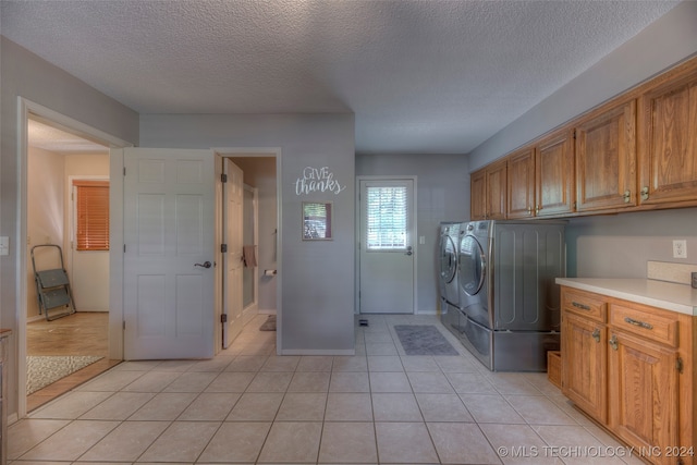 laundry room featuring cabinets, a textured ceiling, light tile patterned flooring, and washing machine and dryer