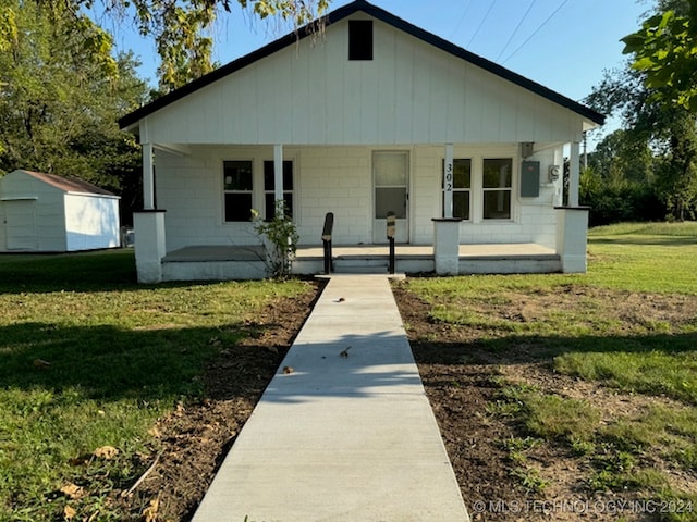 bungalow featuring a front lawn, a storage shed, and covered porch