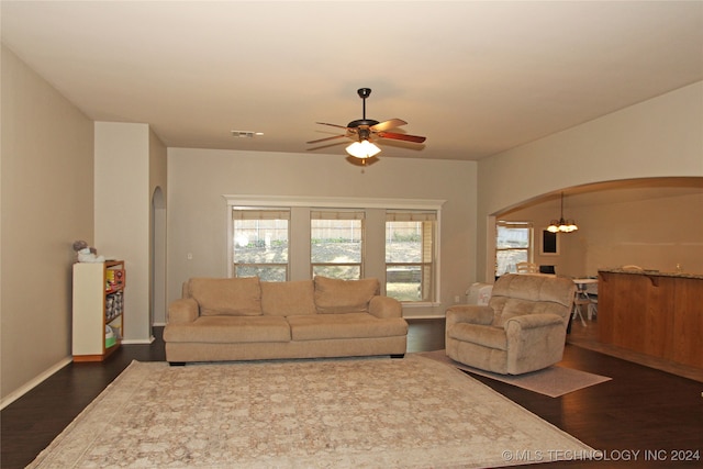 living room featuring ceiling fan with notable chandelier and dark wood-type flooring