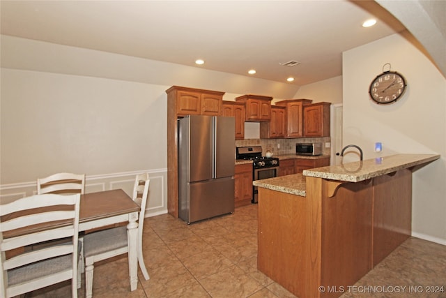 kitchen featuring appliances with stainless steel finishes, decorative backsplash, a kitchen breakfast bar, light tile patterned flooring, and kitchen peninsula