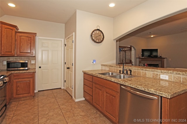 kitchen with light tile patterned floors, sink, stainless steel appliances, light stone countertops, and decorative backsplash