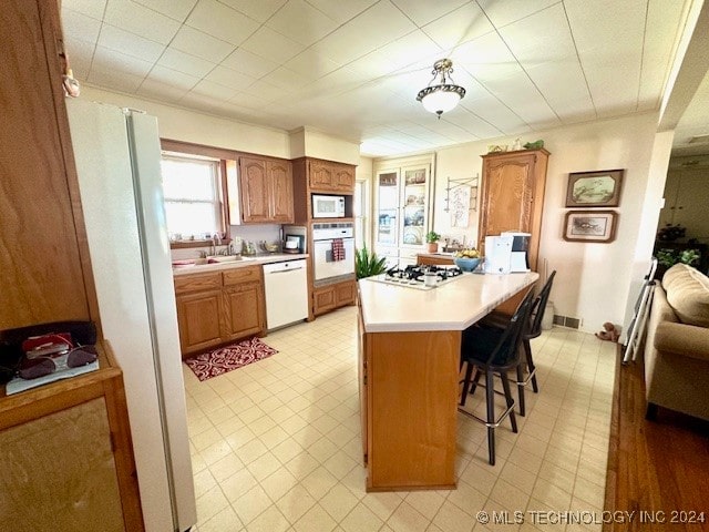 kitchen featuring a breakfast bar, light tile patterned flooring, sink, a kitchen island, and white appliances