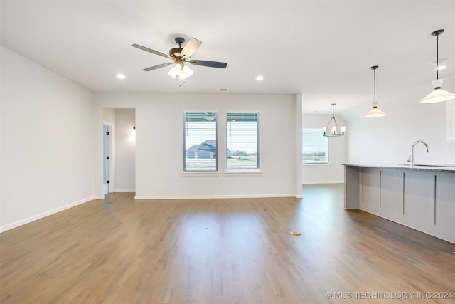 unfurnished living room with ceiling fan with notable chandelier, hardwood / wood-style floors, and sink