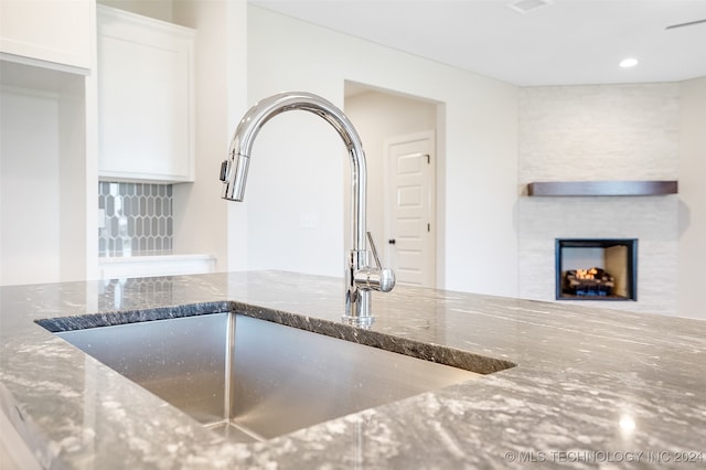 kitchen with stone counters, sink, a large fireplace, and white cabinetry