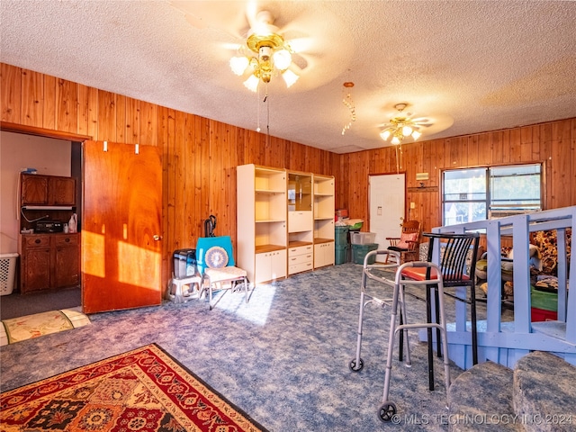 carpeted dining room featuring ceiling fan, wood walls, and a textured ceiling