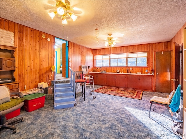 sitting room with carpet flooring, a textured ceiling, ceiling fan, and wooden walls