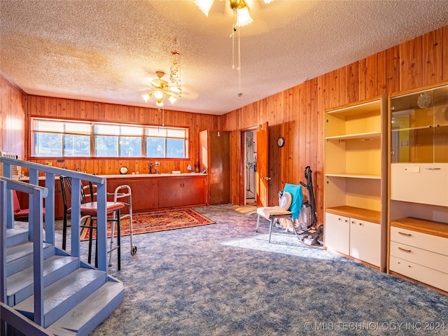 interior space with ceiling fan, wooden walls, carpet, and a textured ceiling