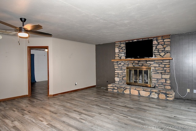 unfurnished living room featuring a textured ceiling, a fireplace, wooden walls, hardwood / wood-style floors, and ceiling fan