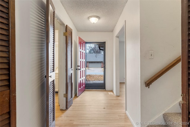 hall with light wood-type flooring, stairs, baseboards, and a textured ceiling