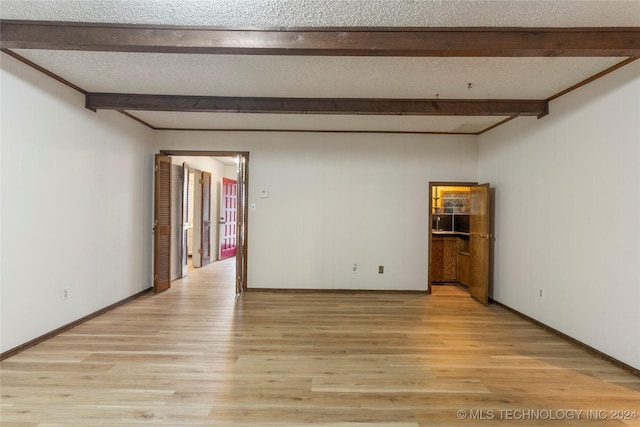 empty room with light hardwood / wood-style flooring, beamed ceiling, and a textured ceiling