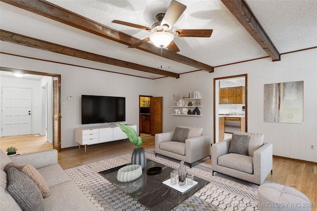 living area featuring baseboards, ceiling fan, wood finished floors, a textured ceiling, and beam ceiling