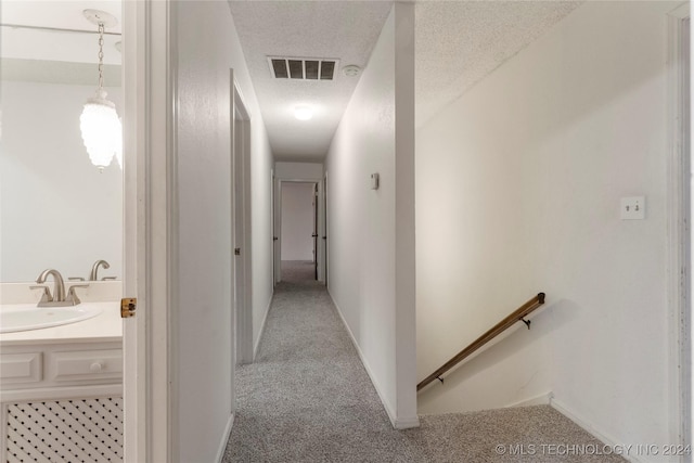 corridor with sink, carpet, and a textured ceiling