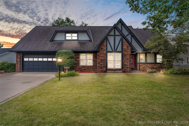 tudor-style house with an attached garage, brick siding, driveway, roof with shingles, and a front yard