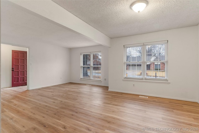 empty room featuring beam ceiling, light hardwood / wood-style floors, and a textured ceiling