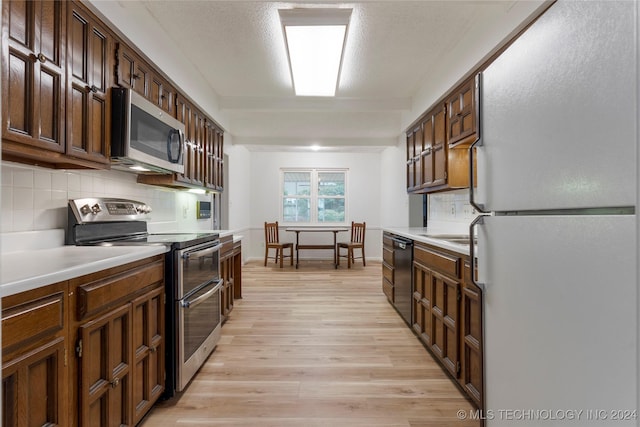 kitchen with tasteful backsplash, light hardwood / wood-style floors, a textured ceiling, dark brown cabinets, and appliances with stainless steel finishes