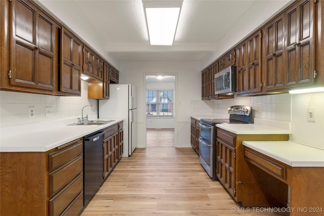 kitchen featuring dark brown cabinetry, sink, light hardwood / wood-style floors, decorative backsplash, and appliances with stainless steel finishes