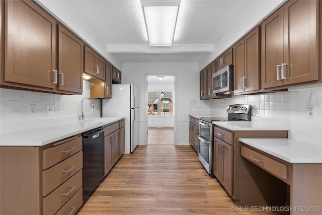 kitchen featuring appliances with stainless steel finishes, light countertops, a sink, and light wood-style flooring