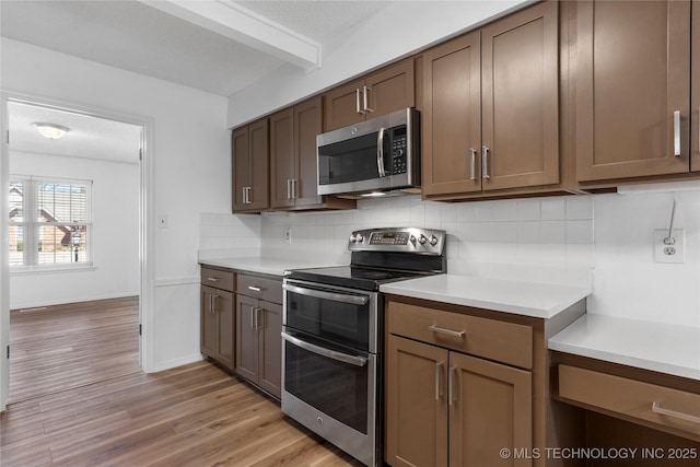 kitchen with light countertops, appliances with stainless steel finishes, light wood finished floors, beamed ceiling, and tasteful backsplash