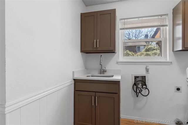 washroom featuring a wainscoted wall, hookup for a washing machine, cabinet space, a sink, and electric dryer hookup