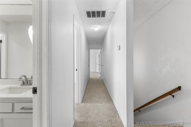 hallway with carpet, a textured ceiling, visible vents, and a sink