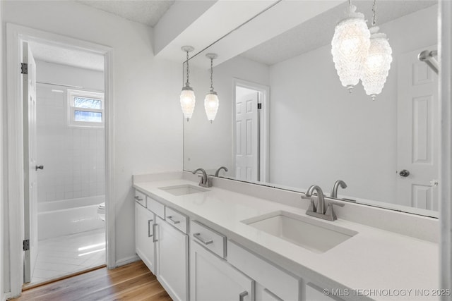 full bathroom featuring double vanity, a sink, a textured ceiling, and wood finished floors