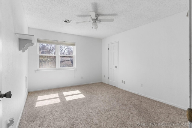 carpeted empty room with baseboards, ceiling fan, visible vents, and a textured ceiling