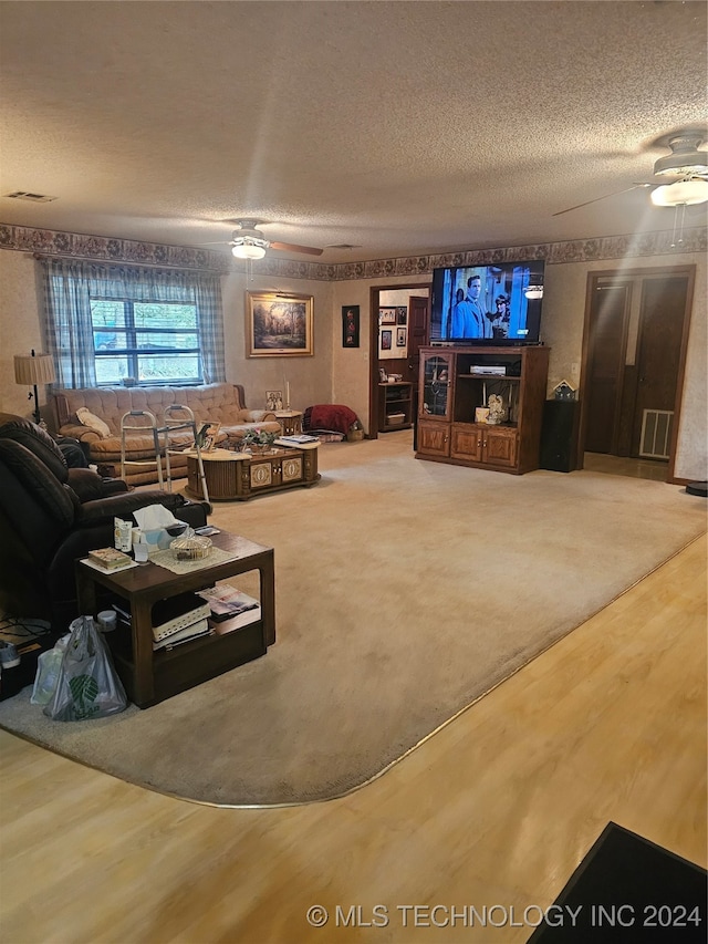 living room with a textured ceiling, wood-type flooring, and ceiling fan