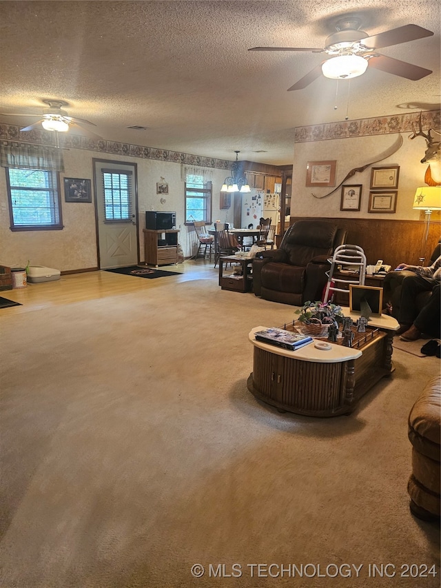 carpeted living room with ceiling fan with notable chandelier, wooden walls, and a textured ceiling