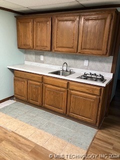 kitchen with light wood-type flooring, stainless steel gas cooktop, sink, and tasteful backsplash