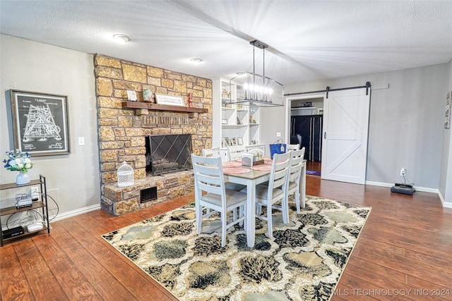 dining room featuring dark wood-type flooring, a barn door, a stone fireplace, a notable chandelier, and a textured ceiling