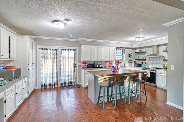 kitchen featuring white cabinetry, stainless steel appliances, wall chimney range hood, dark hardwood / wood-style flooring, and crown molding