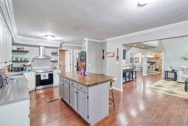 kitchen with white cabinetry, a center island, wall chimney exhaust hood, wood-type flooring, and appliances with stainless steel finishes