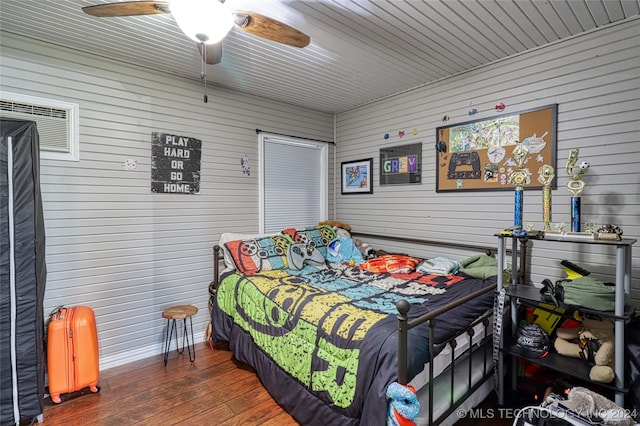 bedroom with ceiling fan, wood walls, and dark hardwood / wood-style flooring