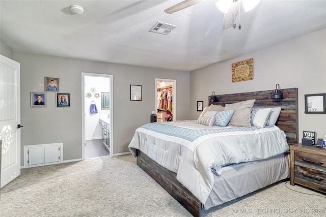 carpeted bedroom with connected bathroom, a walk in closet, a closet, a textured ceiling, and ceiling fan