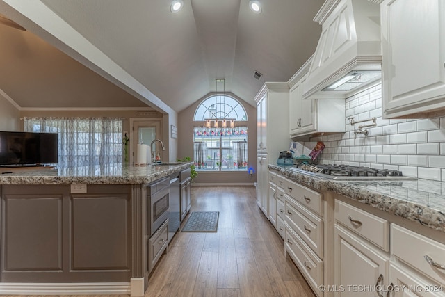 kitchen featuring premium range hood, lofted ceiling, light hardwood / wood-style floors, and white cabinetry