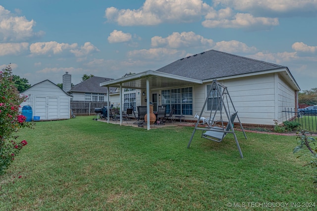 rear view of property featuring a storage unit, a lawn, and a patio