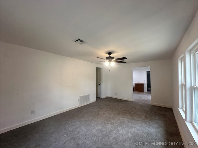 unfurnished room featuring a wealth of natural light, ceiling fan, and dark colored carpet