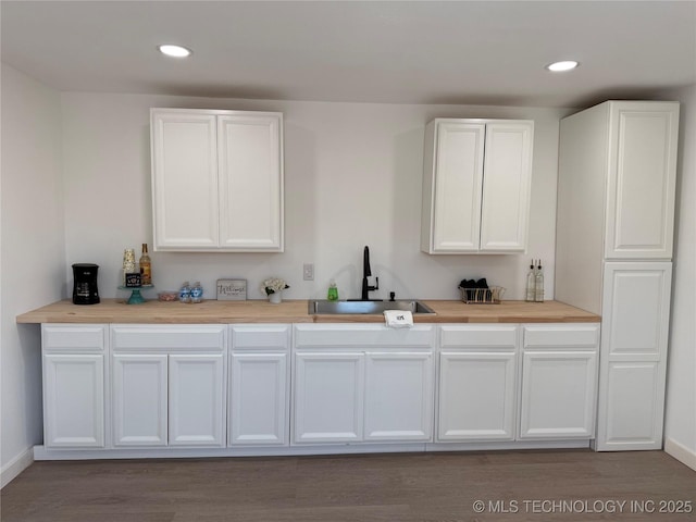 bar with white cabinetry, sink, and wood-type flooring