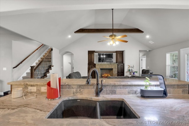 kitchen featuring vaulted ceiling with beams, ceiling fan, a fireplace, and sink