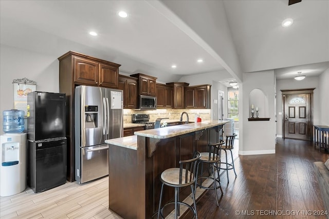 kitchen featuring light stone counters, lofted ceiling, a kitchen island with sink, appliances with stainless steel finishes, and light wood-type flooring