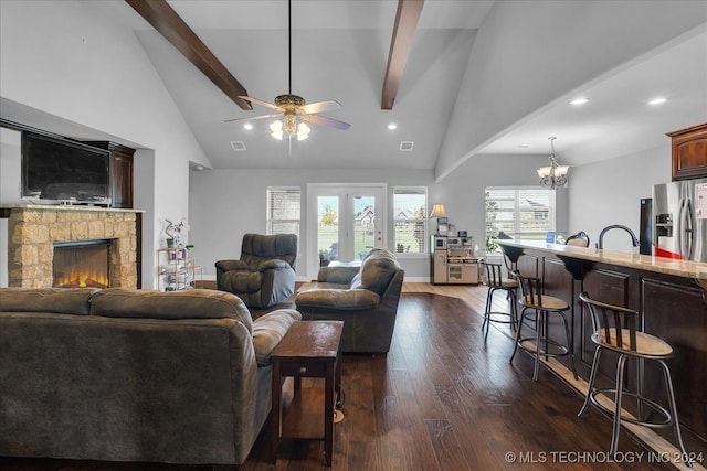 living room featuring high vaulted ceiling, ceiling fan with notable chandelier, a stone fireplace, dark hardwood / wood-style flooring, and beamed ceiling