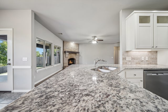 kitchen featuring a stone fireplace, white cabinetry, light stone countertops, and stainless steel dishwasher