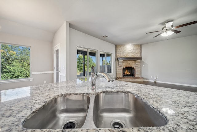 kitchen featuring a stone fireplace, sink, ceiling fan, and light stone counters