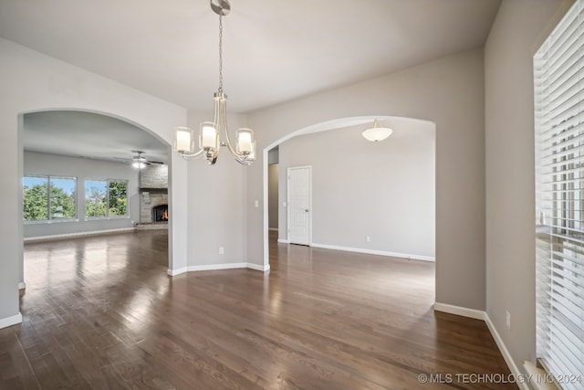 spare room with a stone fireplace, ceiling fan with notable chandelier, and dark hardwood / wood-style flooring