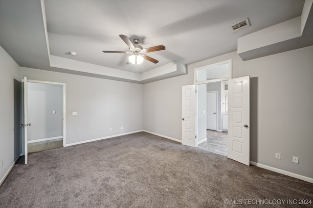 unfurnished bedroom with ceiling fan, a raised ceiling, and dark carpet