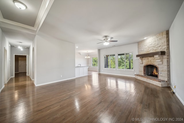 unfurnished living room with ceiling fan with notable chandelier, a fireplace, crown molding, and dark hardwood / wood-style floors