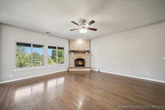 unfurnished living room with a stone fireplace, ceiling fan, and dark hardwood / wood-style flooring