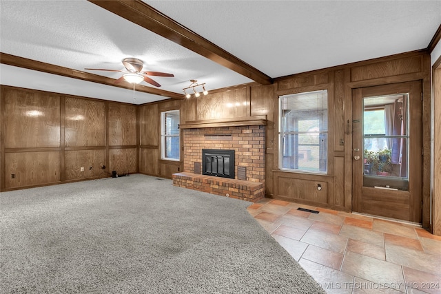 unfurnished living room with a fireplace, wood walls, a textured ceiling, beam ceiling, and ceiling fan